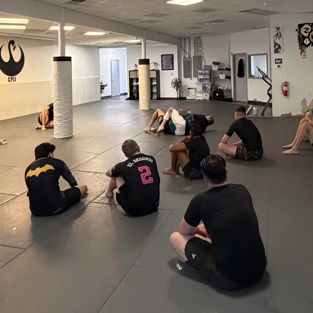 Adults sitting along the mat between rounds during a no-gi class in Norfolk