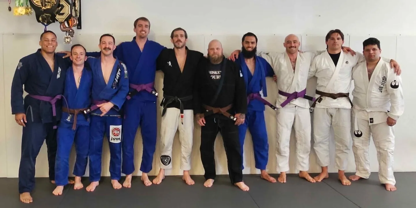 Adult gi jiu jitsu students and their coaches lined up on the mats in Norfolk